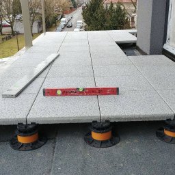 WAWER-BRUK Mariusz Wiącek - Montaż tarasu wentylowanego z płyt betonowych na regulowanych wspornikach, poziomnica na płytach, widok z góry na budynek mieszkalny.