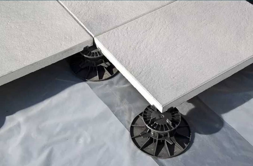 Fragment tarasu wentylowanego z jasnych płyt na regulowanych wspornikach z tworzywa sztucznego, widoczne białe podłoże izolacyjne.