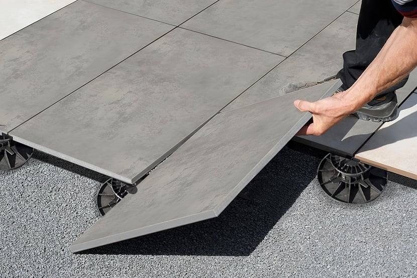 Montaż tarasu wentylowanego z płyt betonowych na regulowanych wspornikach, widoczne podłoże żwirowe i fragment buta montera.