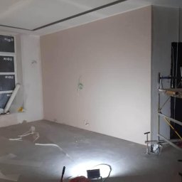 BOHDAN PUSHCHAK DOMINANT - Wnętrze w trakcie prac wykończeniowych: ściana po szpachlowaniu na gładko, z widocznymi puszkami elektrycznymi, sufit z płyt gipsowo-kartonowych z dekoracyjną listwą, na podłodze narzędzia...