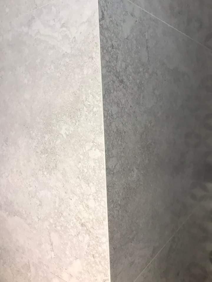 Dwie przylegające do siebie płytki podłogowe: jasnoszara z marmurkowym wzorem i ciemnoszara, tworzące kontrastowe zestawienie.