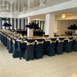 Projekt Event - Uroczysta sala bankietowa z długim stołem w kształcie litery U, nakrytym czarnym obrusem, ze złotymi dekoracjami na krzesłach i stołach, przygotowana na przyjęcie.