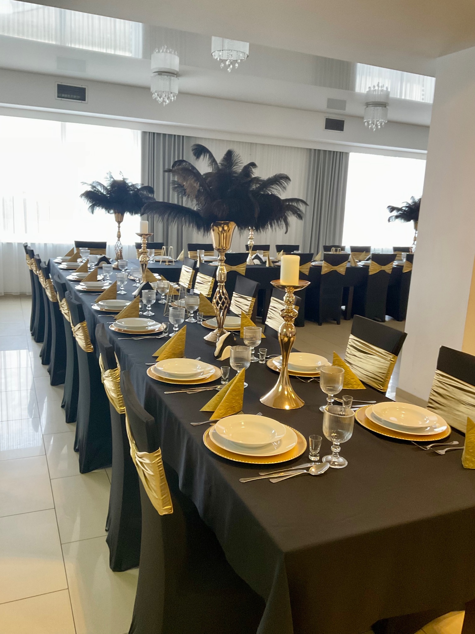 Uroczysty stół weselny w Rozłazinie, nakryty czarnym obrusem, z dekoracjami w kolorze złota, piórami i świecznikami, przygotowany na przyjęcie.