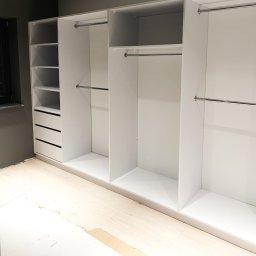 MILAR PROJEKT Waldemar Kruszelnicki - Biała szafa wnękowa z półkami i drążkami na ubrania, widoczne niedokończone panele podłogowe.