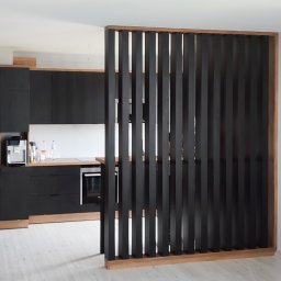 MILAR PROJEKT Waldemar Kruszelnicki - Nowoczesna kuchnia z czarnymi frontami i drewnianym blatem, oddzielona od reszty pomieszczenia ażurową, drewnianą ścianką działową z pionowych listew.