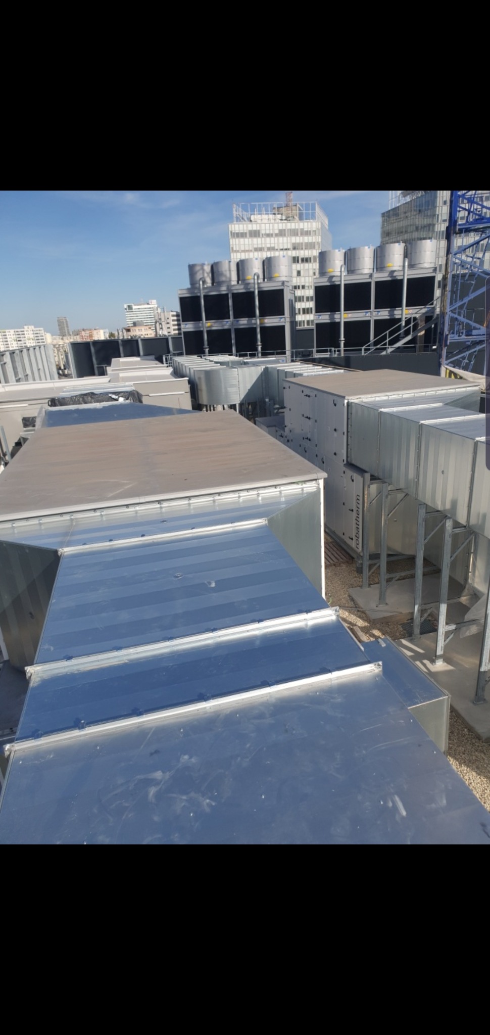 Instalacja wentylacyjna na dachu budynku komercyjnego, widoczne metalowe kanały wentylacyjne, centrala wentylacyjna oraz chłodnice wentylacyjne w tle, widok z góry w słoneczny dzień.