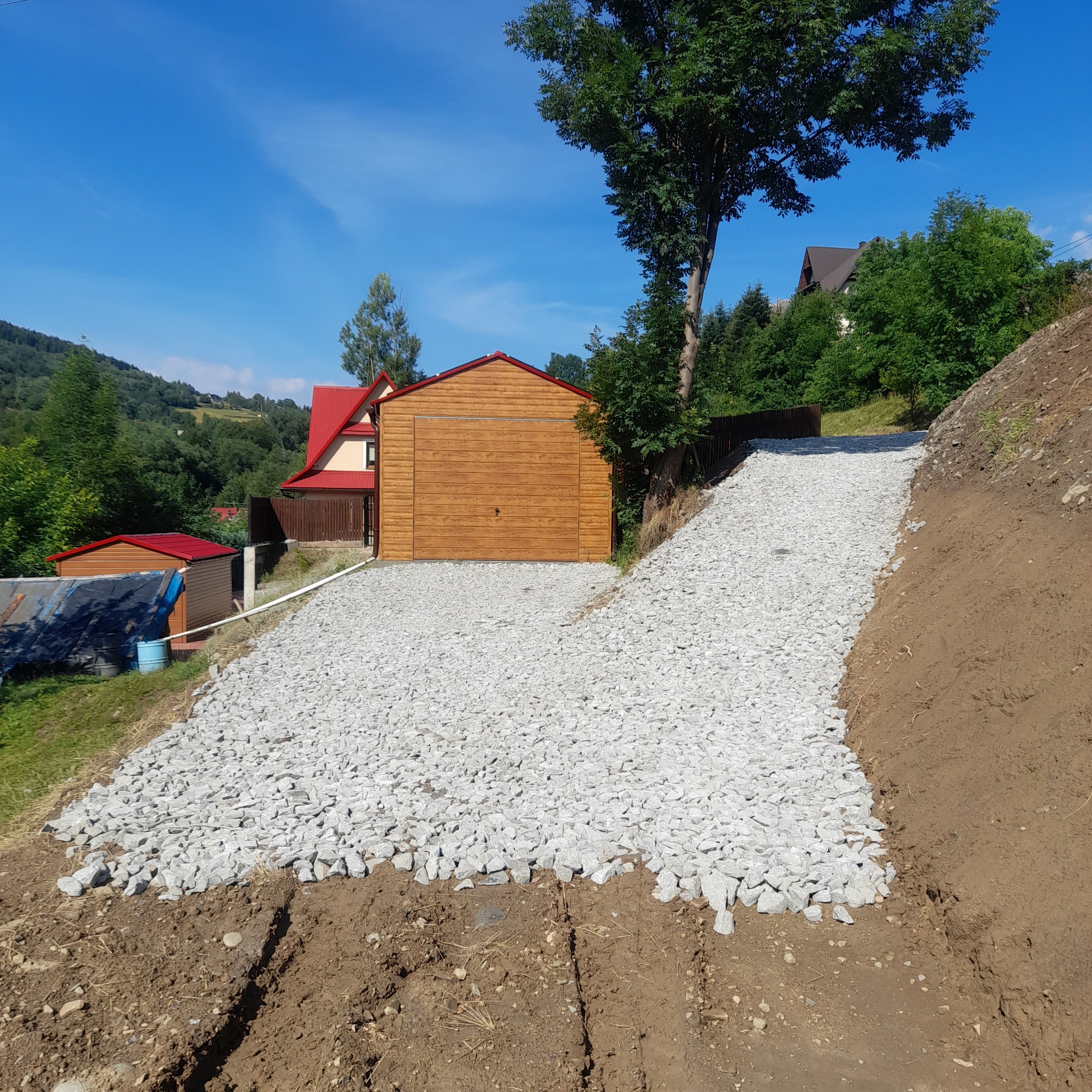 Utwardzona, kamienista droga prowadząca do drewnianego garażu na wzgórzu w słoneczny dzień.