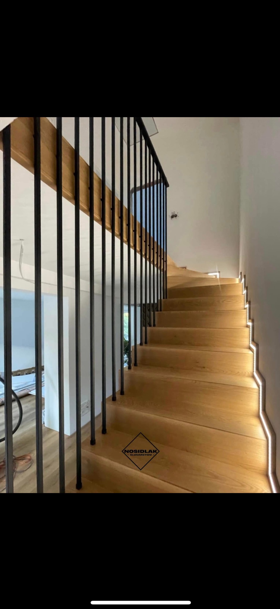 Drewniane schody z czarną, metalową balustradą i subtelnym oświetleniem LED wzdłuż stopni.