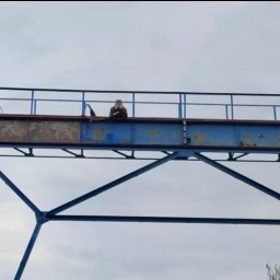 Eco Blast System Walczak Spółka Jawna - Pracownik na konstrukcji stalowej mostu dźwigowego przygotowuje powierzchnię do malowania, widoczne ślady korozji i częściowo oczyszczona powierzchnia.