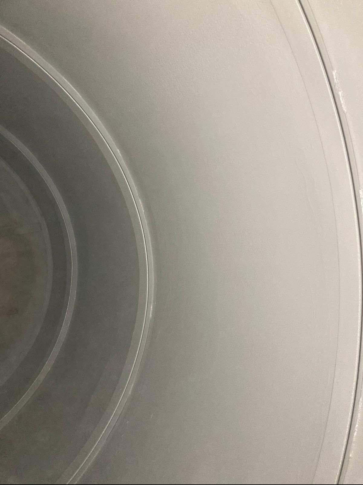 Metalowa powierzchnia po piaskowaniu, widoczne okręgi i gładka faktura. Jasnoszary odcień, delikatne odbicia światła. Detal obróbki.