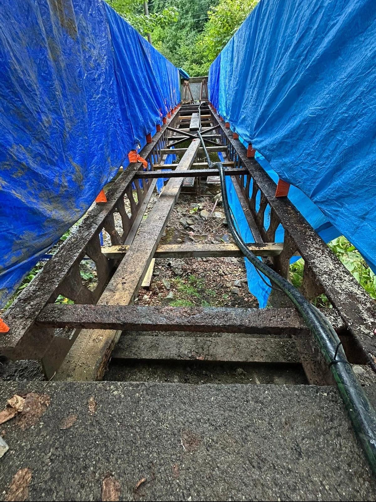 Przygotowanie do piaskowania konstrukcji: rusztowanie z osłonami z niebieskiej plandeki, widoczne ślady rdzy i zabrudzeń. Ujęcie z dołu, perspektywa zbieżna.