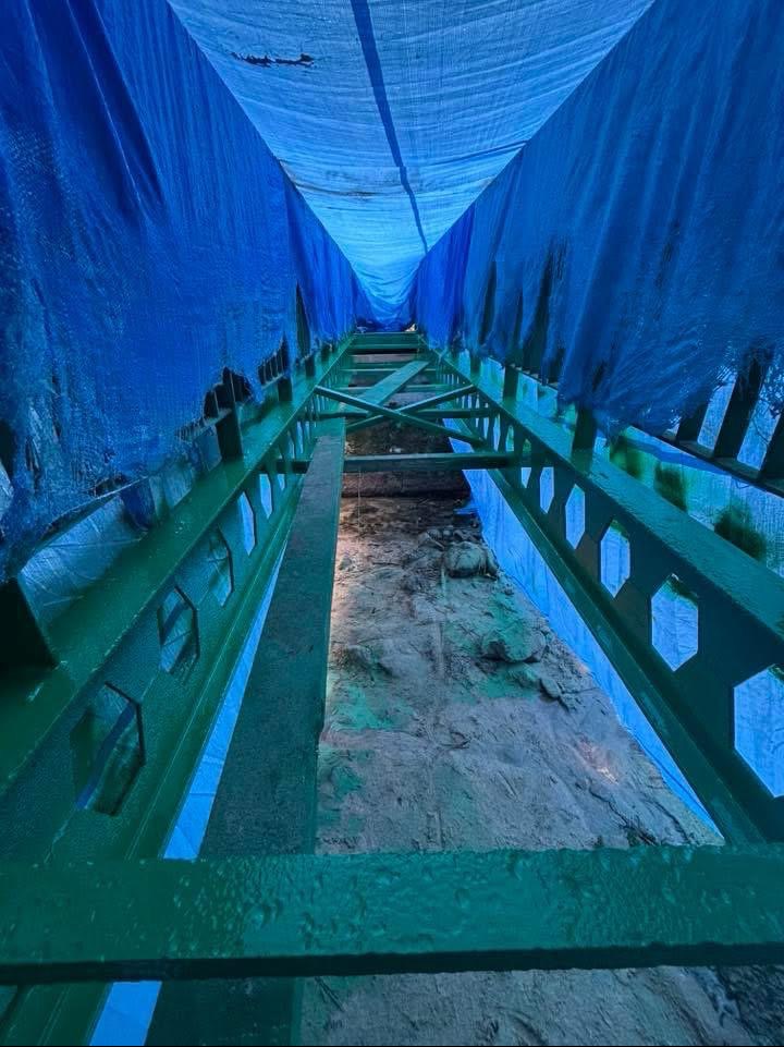 Oczyszczona konstrukcja stalowa mostu, zabezpieczona plandeką. Widoczne ślady piaskowania i świeża, zielona farba antykorozyjna. Ujęcie z dołu, perspektywa tunelu.