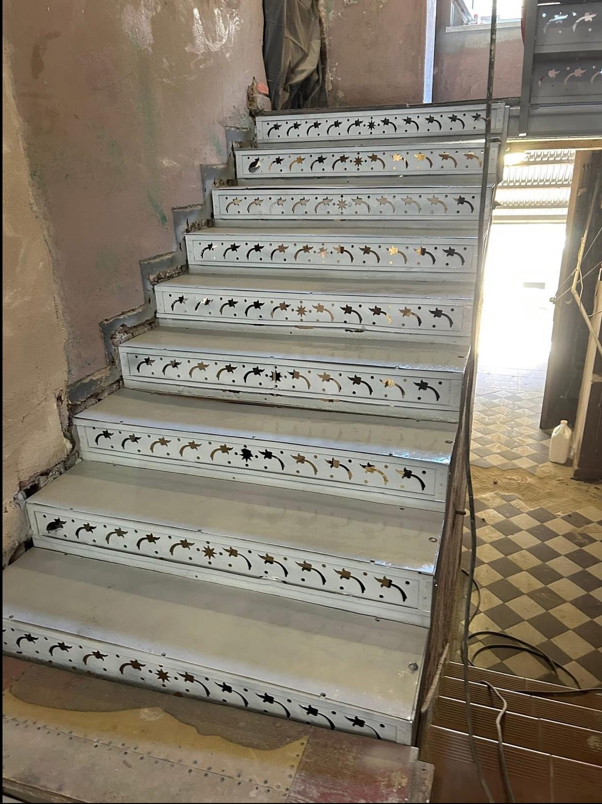 Odnowione schody z dekoracyjnym wzorem, po usunięciu starych powłok. Widoczne detale zdobień i kontrast między odnowioną powierzchnią a surowym otoczeniem.