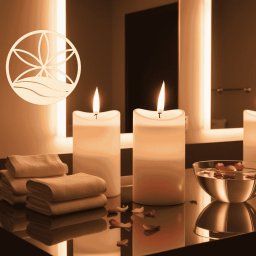 FELIZ SPÓŁKA Z OGRANICZONĄ ODPOWIEDZIALNOŚCIĄ - Relaksująca aranżacja spa w Gdańsku: płonące świece, stos ręczników i miseczka z płatkami róż na lustrzanej powierzchni, podświetlane lustra w tle, logo salonu w lewym górnym rogu.