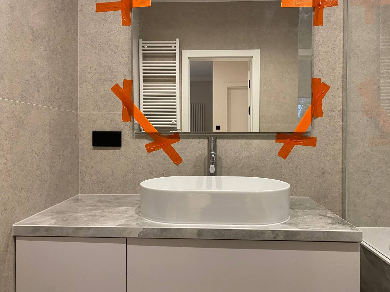 Nowoczesna łazienka z owalną umywalką nablatową, lustrem zabezpieczonym taśmą malarską i grzejnikiem drabinkowym w tle.