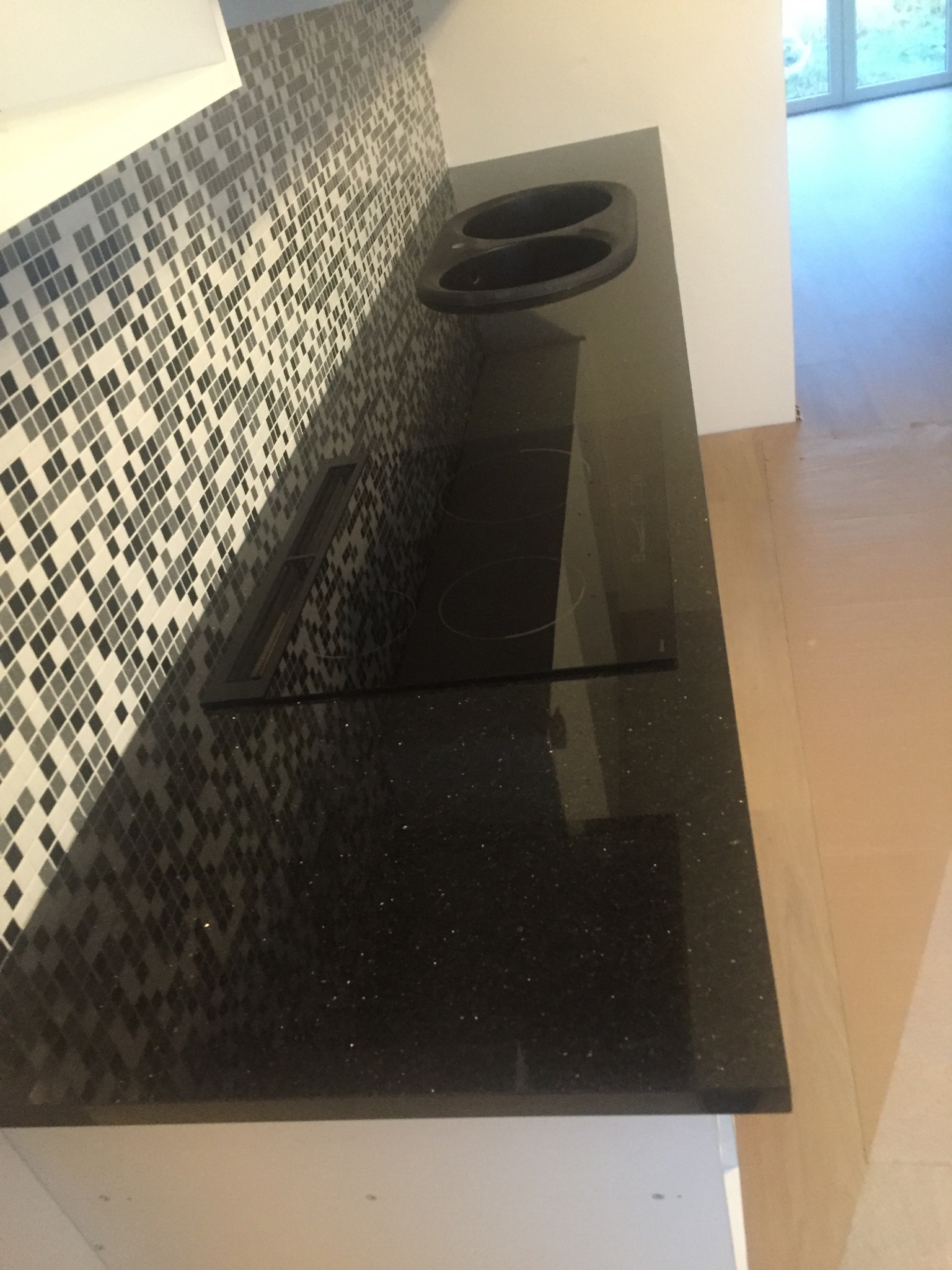 Błyszczący, czarny blat z wbudowaną płytą indukcyjną i zlewem w kuchni we Włocławku, wykończony mozaiką na ścianie.