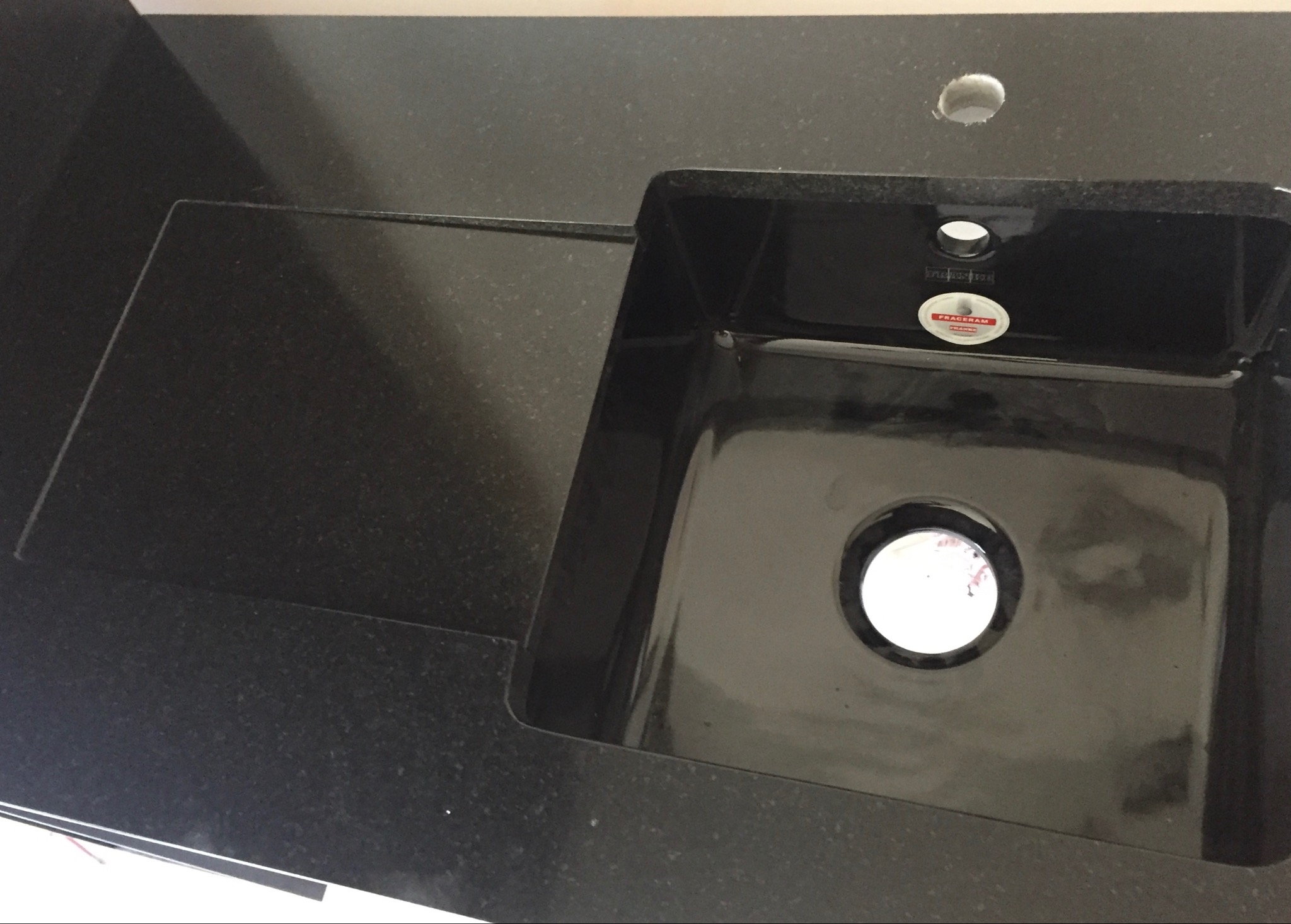 Czarny, kamienny blat kuchenny z wbudowanym, czarnym zlewem i otworem na baterię. Widoczne delikatne refleksy światła na powierzchni kamienia.