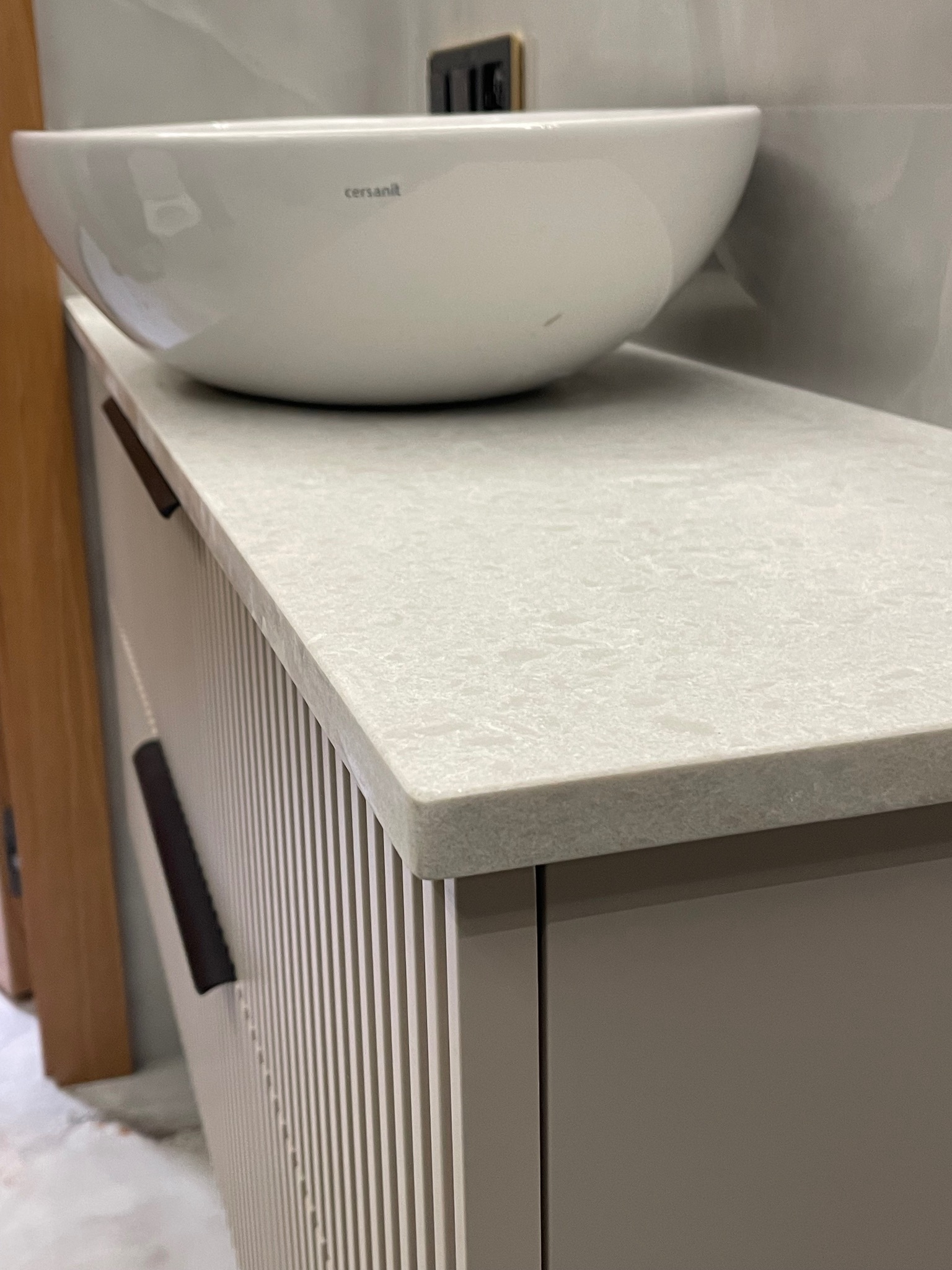 Jasny blat z konglomeratu w łazience z umywalką Cersanit. Ujęcie z bliska, ukazujące strukturę blatu i detale szafki z ryflowanymi frontami.