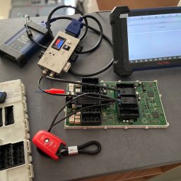 Codena Motors Patryk Płomiński - Diagnostyka sterownika samochodowego BMW za pomocą testera diagnostycznego Autel, z widoczną płytką drukowaną, przewodami i kluczykami, wskazując na proces pobierania informacji.