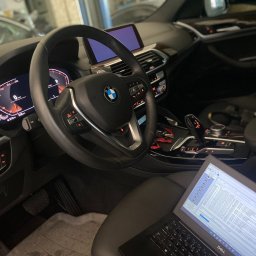 Codena Motors Patryk Płomiński - Wnętrze samochodu BMW z włączonym laptopem wyświetlającym diagnostykę pojazdu, widoczne deska rozdzielcza, kierownica z logo BMW i ekran nawigacji.