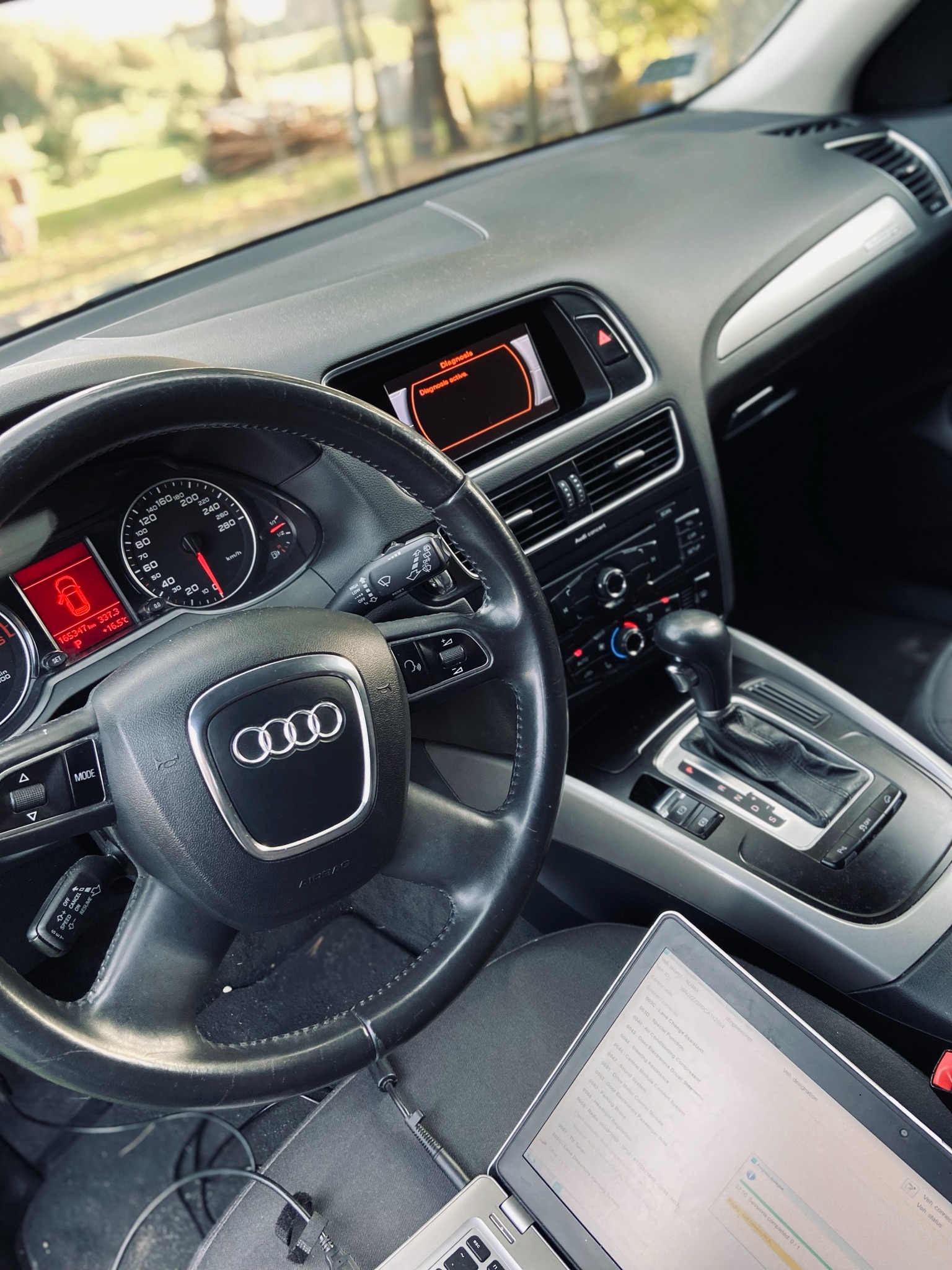 Wnętrze samochodu Audi z widocznym ekranem diagnostycznym laptopa podłączonego do systemu pojazdu, prezentującym listę modułów i parametrów, co sugeruje proces diagnostyki lub naprawy.