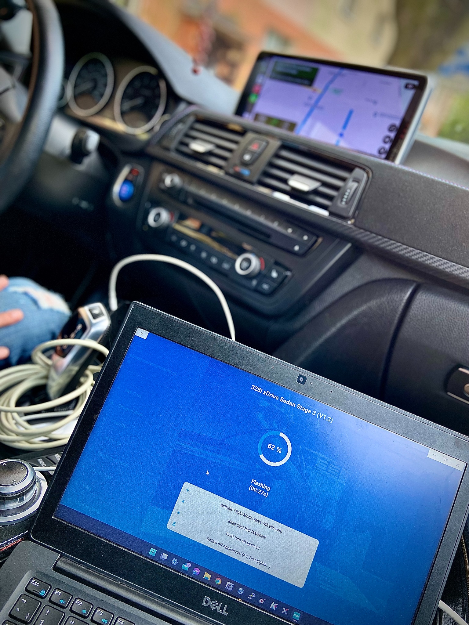 Wnętrze samochodu BMW 328i xDrive Sedan z laptopem Dell na desce rozdzielczej, na ekranie widoczny proces flashowania oprogramowania Stage 3, tablet z nawigacją zamontowany powyżej deski rozdzielczej.