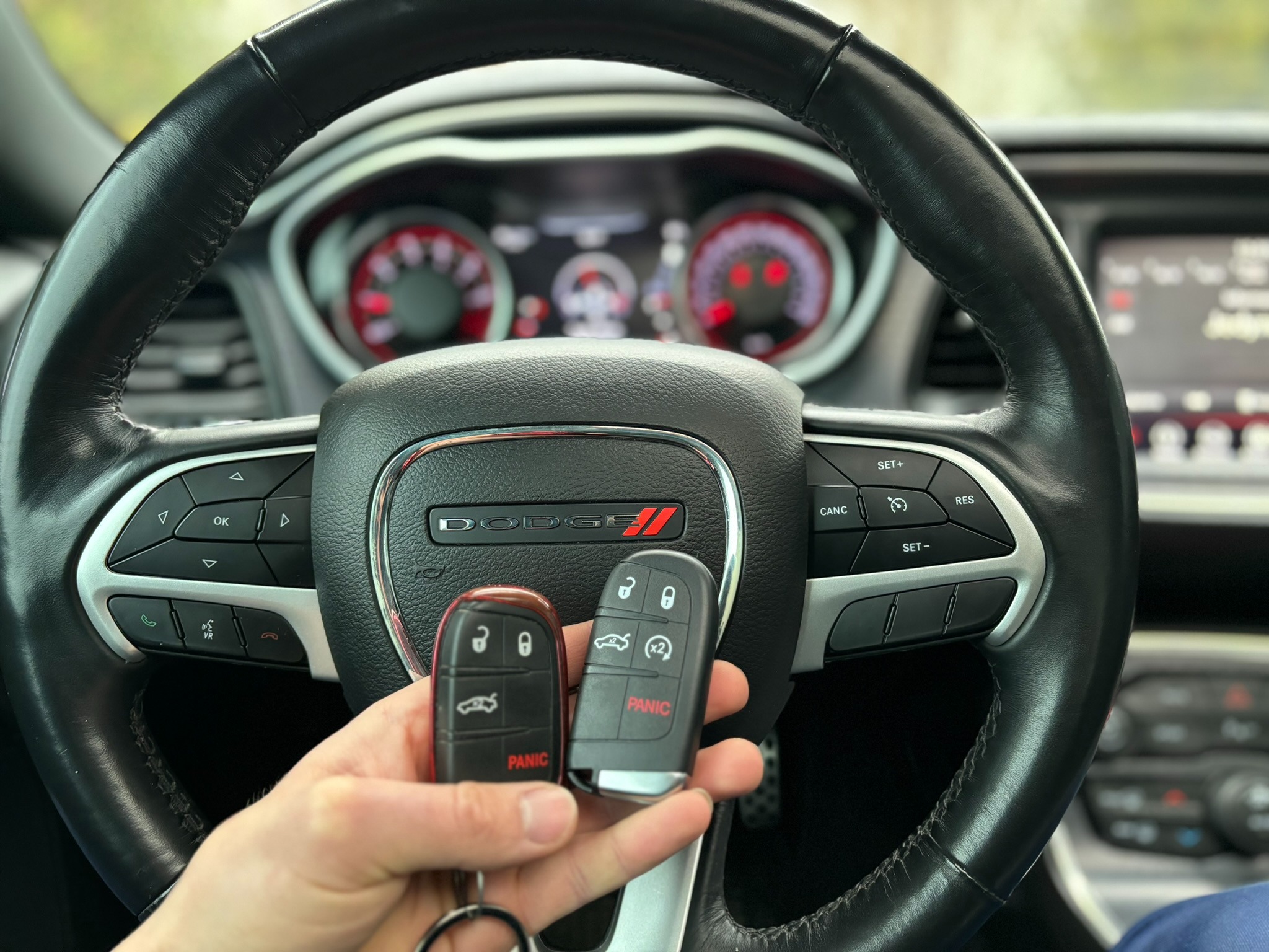 Dwie różne wersje kluczyków samochodowych Dodge trzymane w dłoni na tle kierownicy Dodge Challenger z widocznym logo i deską rozdzielczą.