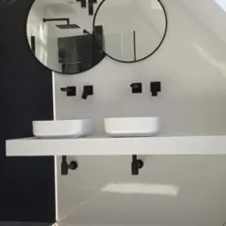 Nowoczesna łazienka w bieli i czerni z dwoma okrągłymi lustrami, minimalistycznymi umywalkami nablatowymi i czarną armaturą, pod skosem dachu.