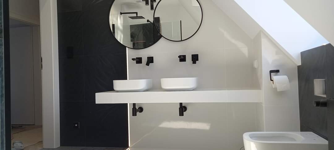 Nowoczesna łazienka w bieli i czerni z dwoma okrągłymi lustrami, minimalistycznymi umywalkami nablatowymi i czarną armaturą, pod skosem dachu.