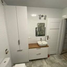 Starz-Drew - Nowoczesna łazienka z białą szafką pod umywalką z drewnianym blatem, lustrem w czarnej ramie, białą szafą i płytkami z subtelnym wzorem fal.