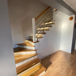 Starz-Drew - Nowoczesne schody z podświetlanymi stopniami, drewniane stopnie i białe podstopnice, balustrada ze stali nierdzewnej, zabudowa pod schodami z białymi frontami, drewniana podłoga.