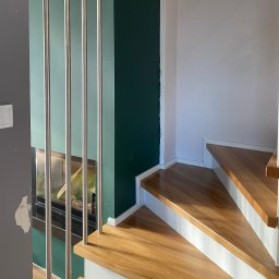 Starz-Drew - Fragment drewnianych schodów z metalową balustradą na tle ściany w kolorze butelkowej zieleni i akwarium.