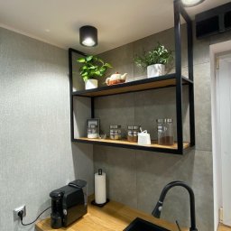 Starz-Drew - Półka kuchenna z drewnianymi blatami i czarną metalową ramą, na której stoją przyprawy w słoikach, doniczki z roślinami i czajnik, z widocznym ekspresem do kawy na blacie.