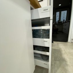 Starz-Drew - Wysuwana, trzypoziomowa szuflada cargo marki Blum w białej zabudowie kuchennej, wypełniona szklanymi miskami i talerzami.