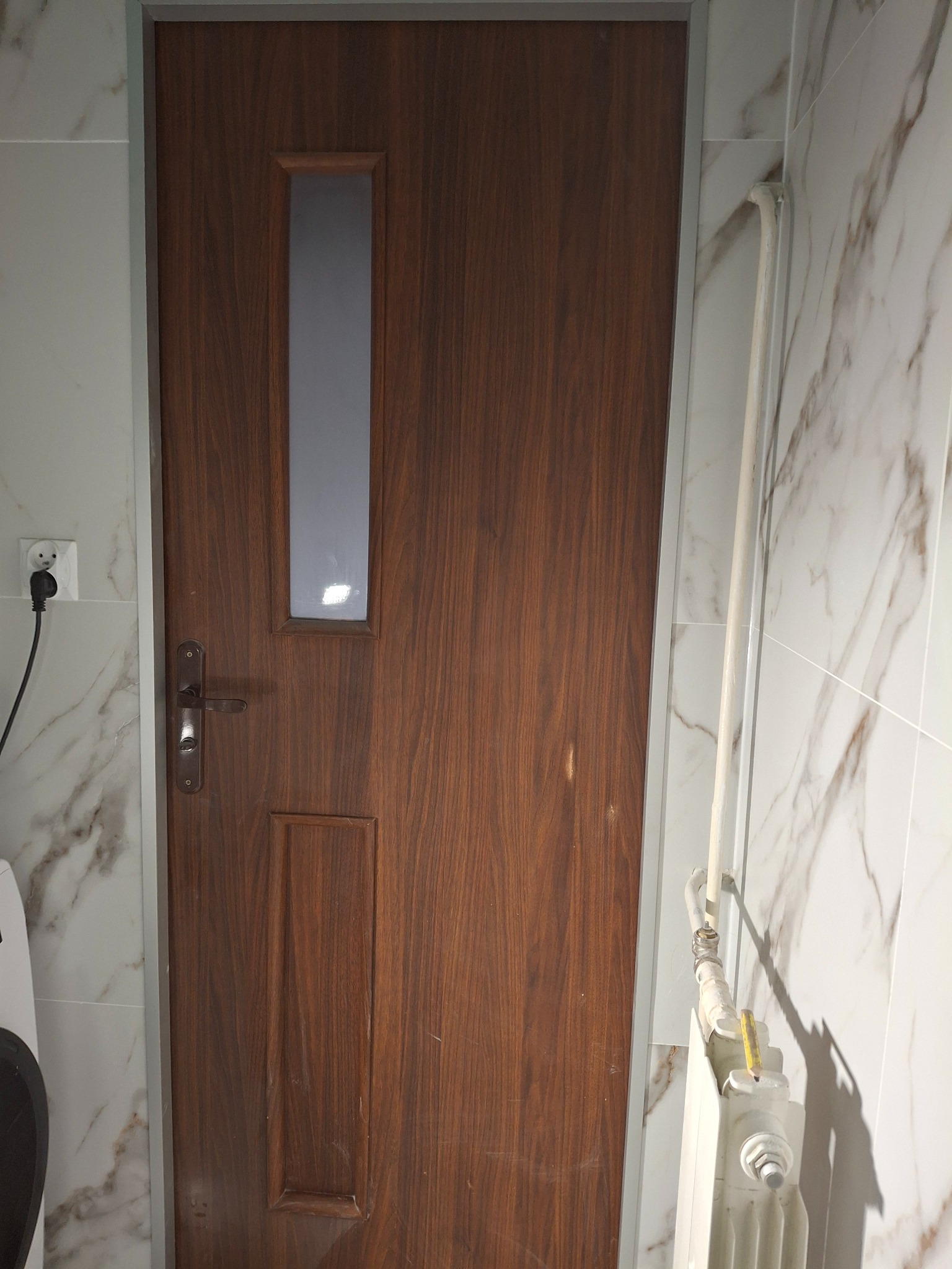 Drewniane drzwi wewnętrzne z szybką, zamontowane w łazience z marmurowymi płytkami, obok biały grzejnik i widoczny fragment pralki.