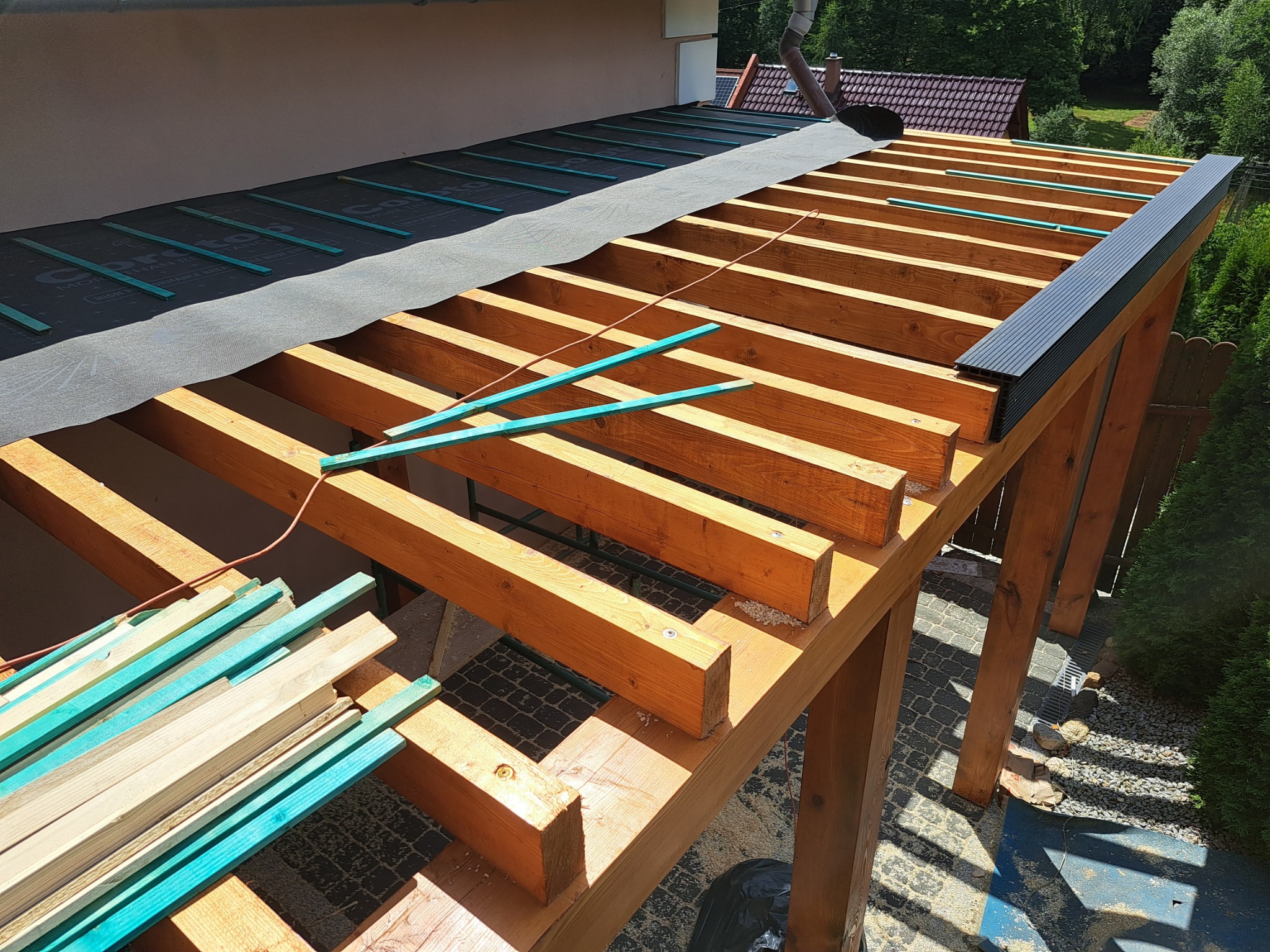 Konstrukcja drewniana dachu w trakcie budowy, widoczne krokwie, membrana dachowa z listwami kontrującymi, przygotowane deski pomalowane na turkusowo, elementy obróbki blacharskiej