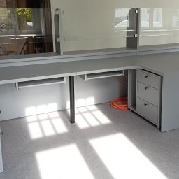 Andrii Pavlov - Szara, narożna szafa biurowa na wymiar z szklaną nadstawką, widok z boku,  z elementami szuflad i wysuwanymi półkami na klawiaturę, kabel w tle.