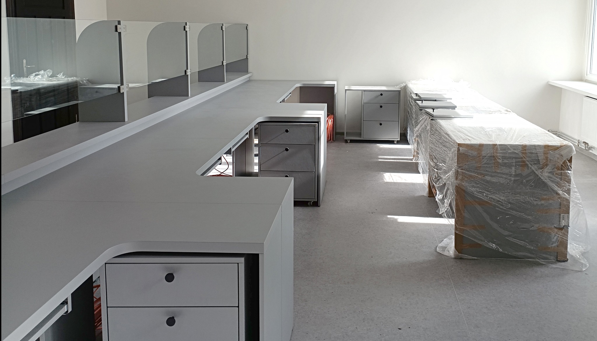 Białe biurko z przegrodami i szufladami w Olesno, częściowo jeszcze zabezpieczone folią. Nowoczesne meble biurowe po montażu, jasne wnętrze, widok z perspektywy.