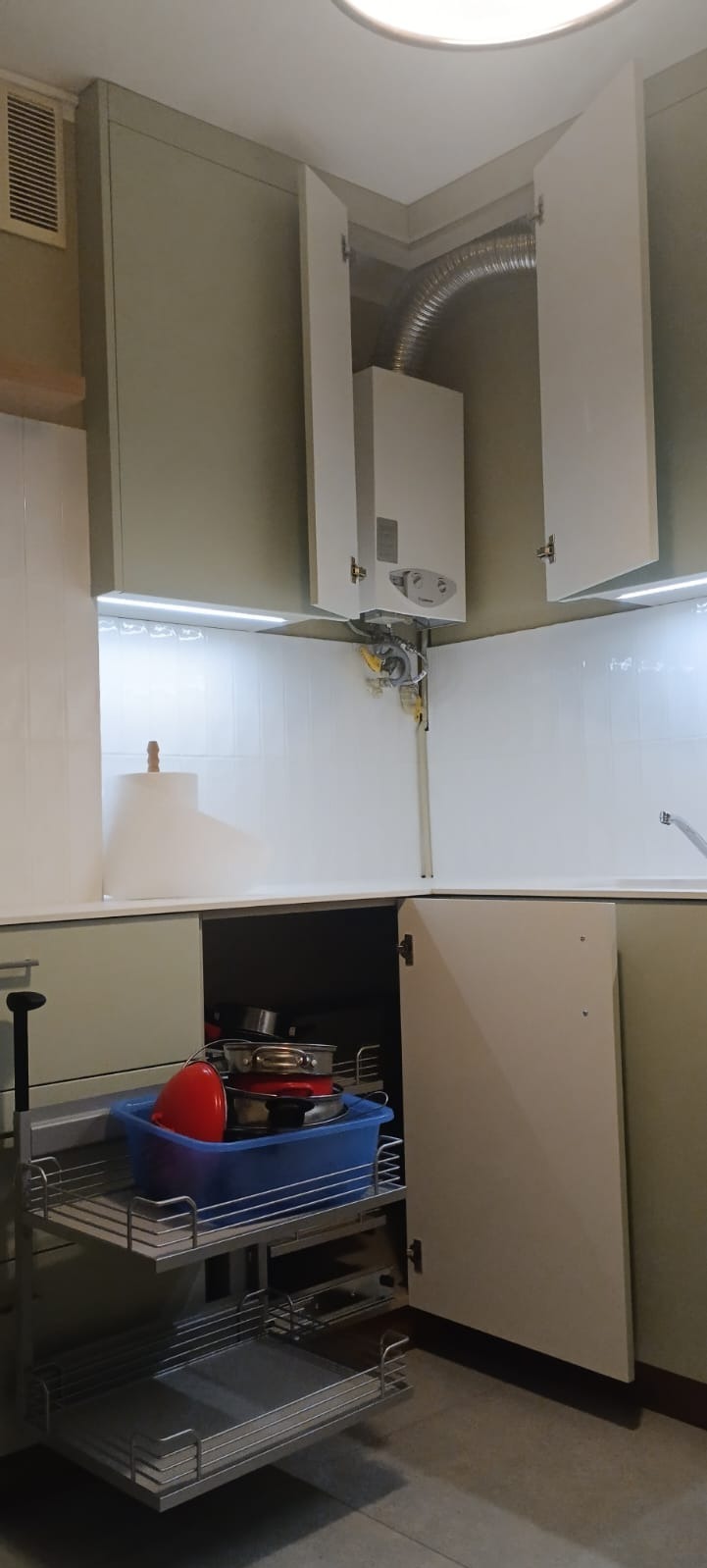 Jasna kuchnia z szafkami, otwartą szafką narożną z wysuwanym koszem na naczynia i piecem gazowym w szafce wiszącej. Oświetlenie LED pod szafkami.