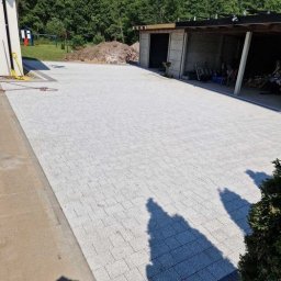 Karol Piątkowski - Ułożona jasnoszara kostka brukowa na dużej powierzchni podwórza w Słupsku, widoczny budynek gospodarczy i plac zabaw w tle.