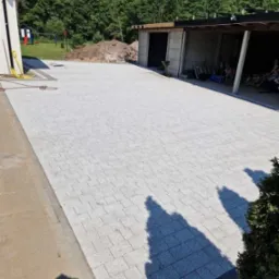 Ułożona jasnoszara kostka brukowa na dużej powierzchni podw&oacute;rza w Słupsku, widoczny budynek gospodarczy i plac zabaw w tle.