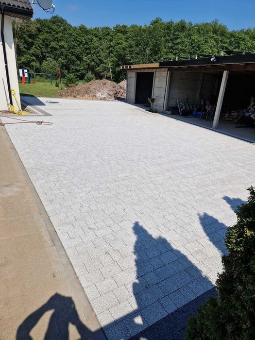 Ułożona jasnoszara kostka brukowa na dużej powierzchni podwórza w Słupsku, widoczny budynek gospodarczy i plac zabaw w tle.