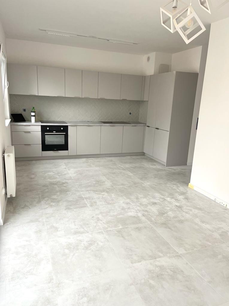 Jasna kuchnia w minimalistycznym stylu z szarymi szafkami, płytkami chevron nad blatem i nowoczesną lampą sufitową