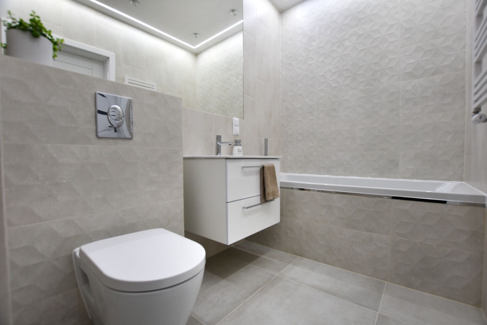 Nowoczesna łazienka z geometrycznymi płytkami, podwieszana toaleta i szafka z umywalką, lustro z oświetleniem LED, minimalistyczny design.