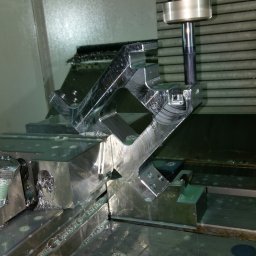 MECAMA SPÓŁKA Z OGRANICZONĄ ODPOWIEDZIALNOŚCIĄ - Obróbka CNC detalu o skomplikowanym kształcie z użyciem chłodziwa, widoczny frez i mocowanie w uchwycie maszyny.