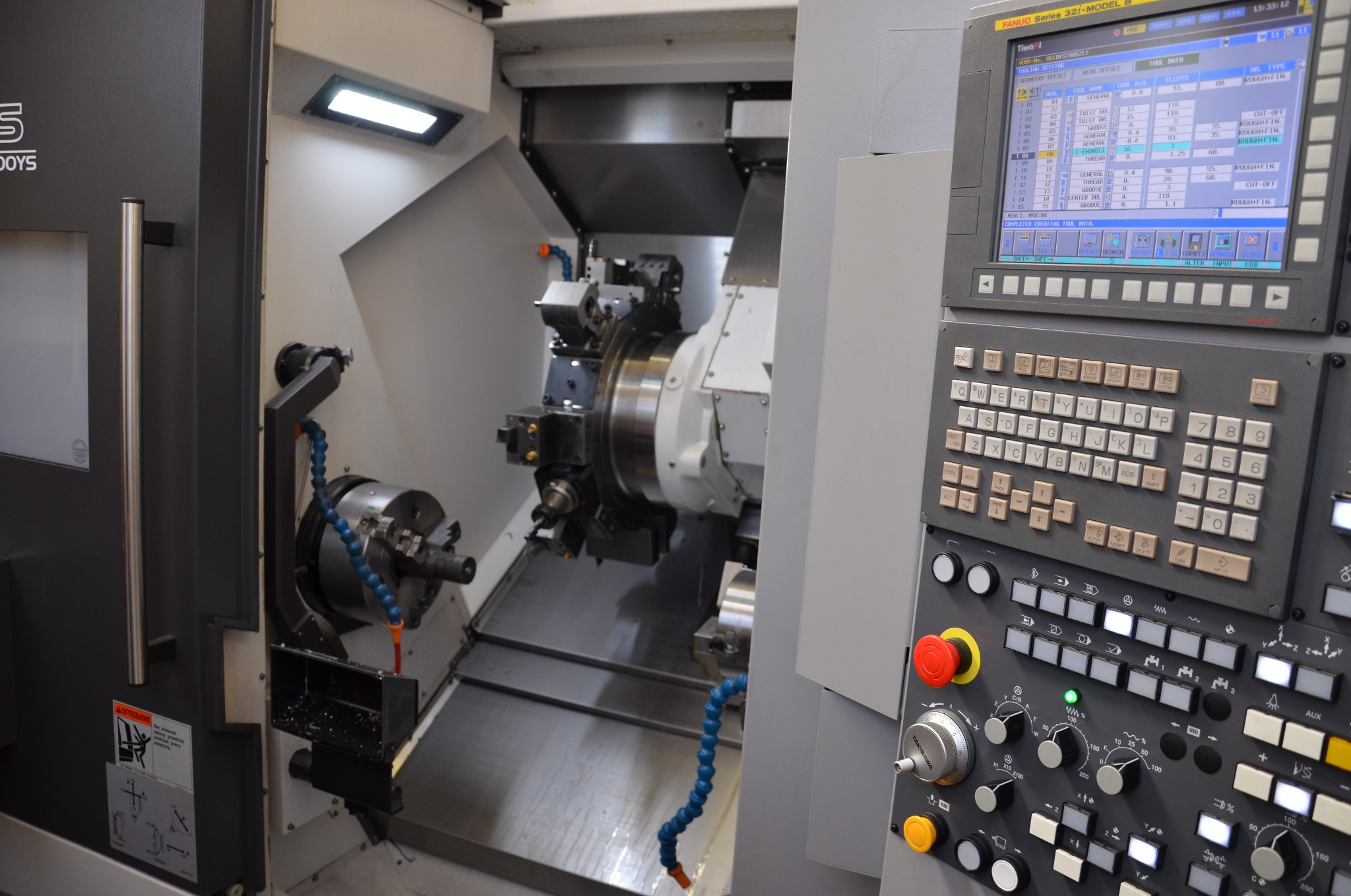 Wnętrze nowoczesnej tokarki CNC z widocznym uchwytem, narzędziami i panelem sterowania Fanuc Series 32i-MODEL B.