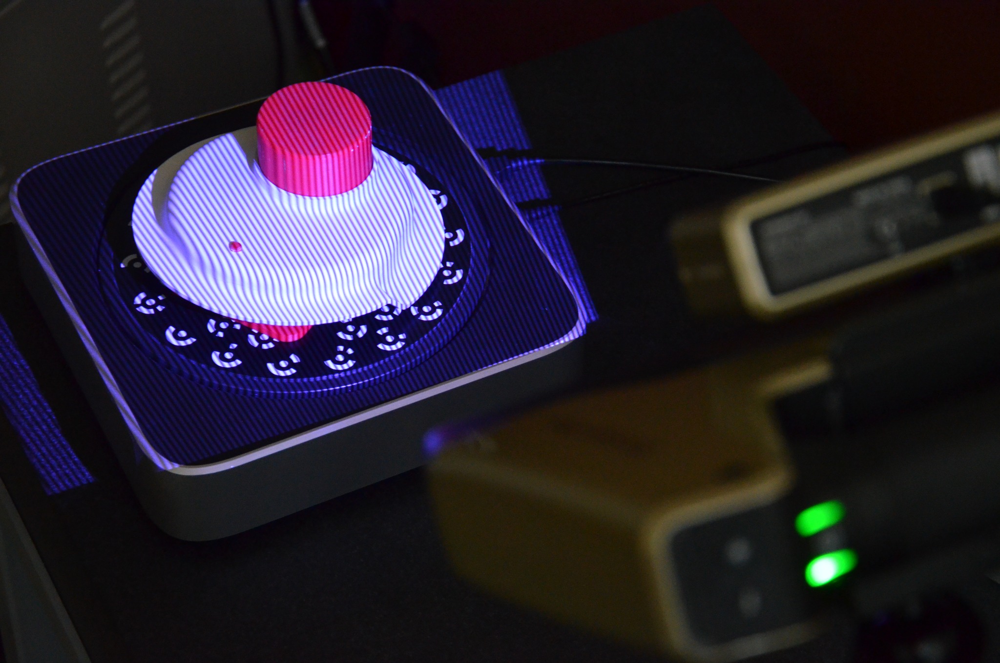 Skanowanie 3D obiektu z użyciem skanera 3D, widoczne światło strukturalne na powierzchni modelu, w tle fragment urządzenia skanującego.