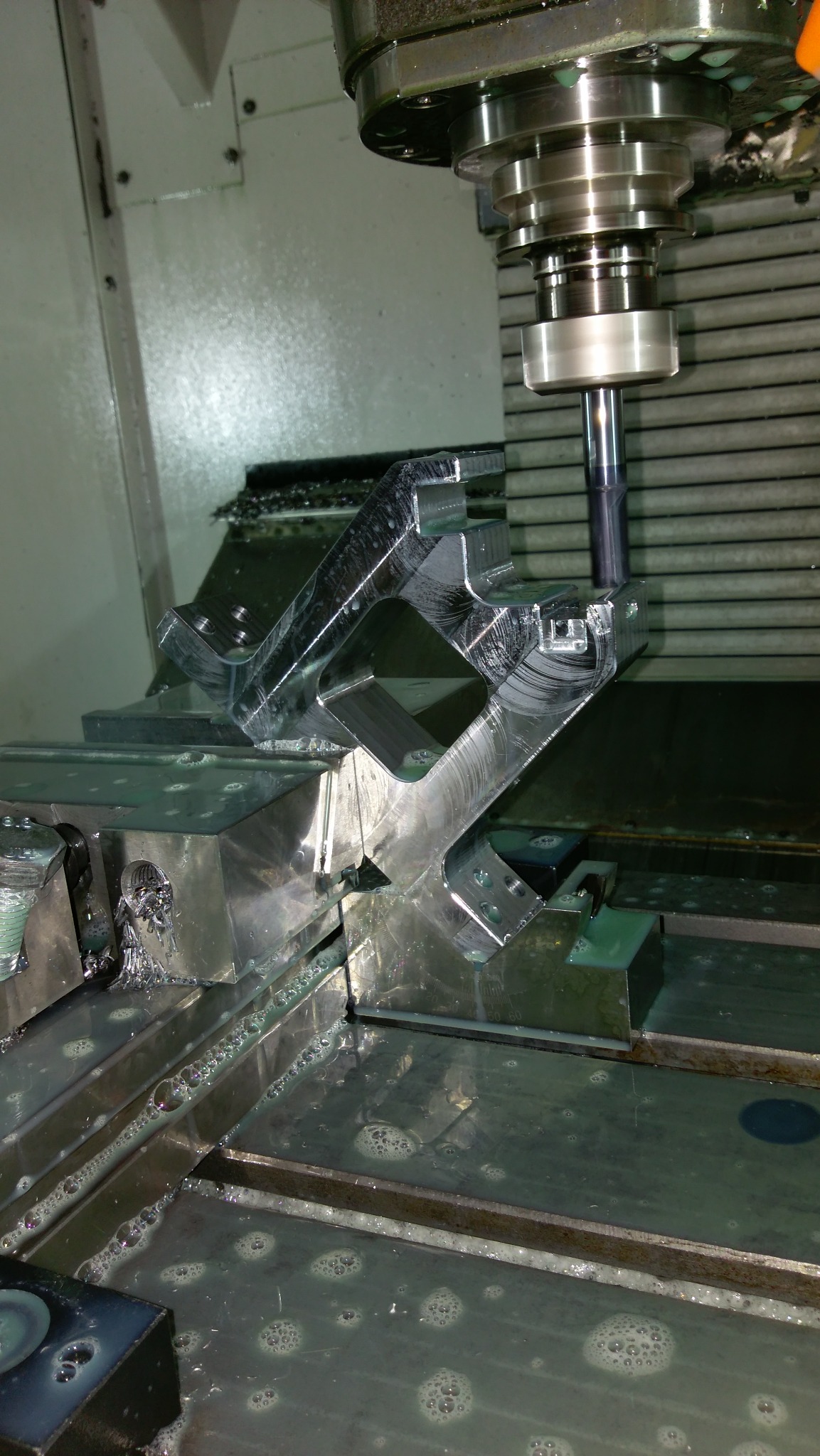 Obróbka CNC detalu o skomplikowanym kształcie z użyciem chłodziwa, widoczny frez i mocowanie w uchwycie maszyny.