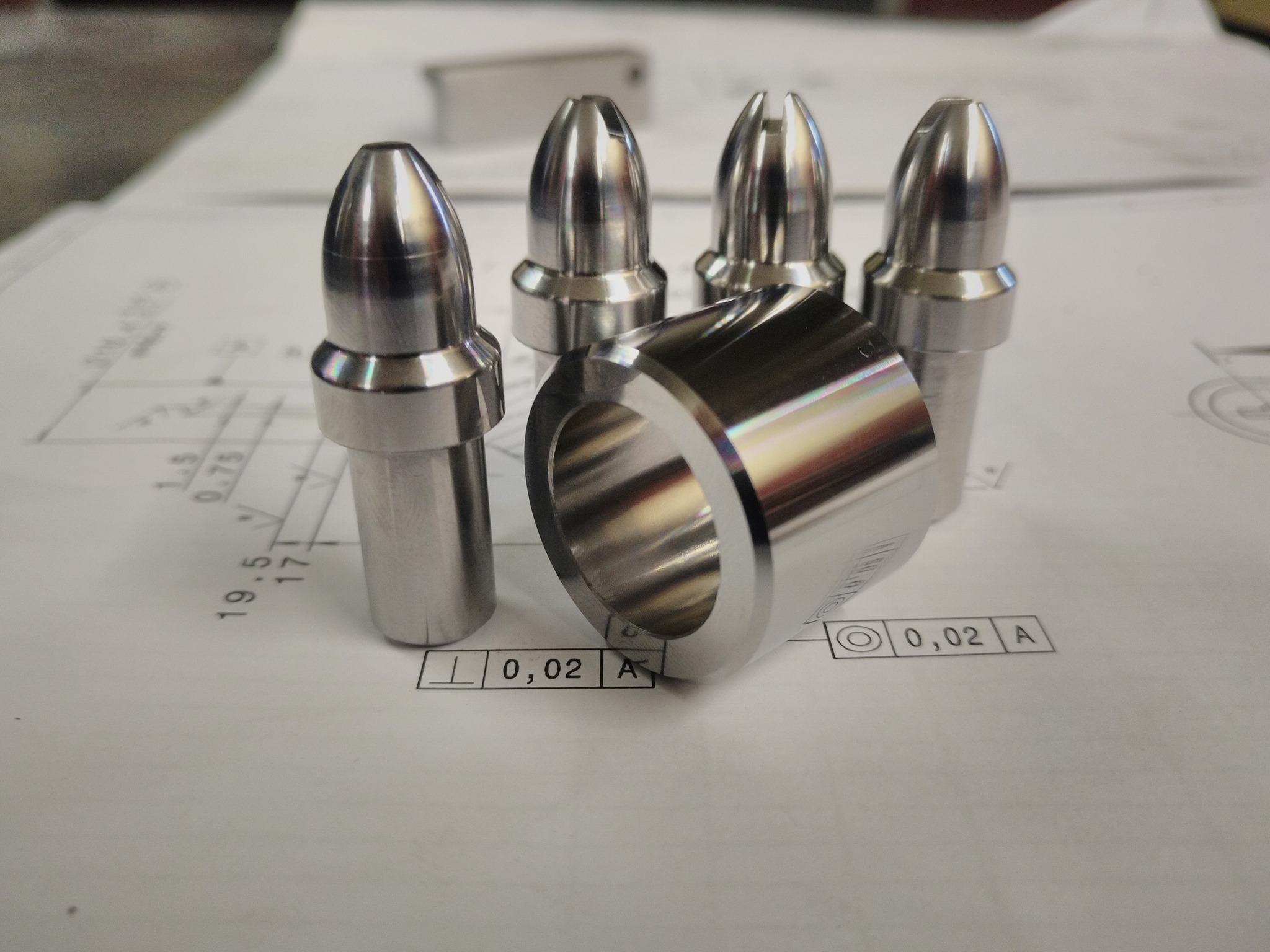 Precyzyjnie obrobione, metalowe elementy na rysunku technicznym w Chorzowie: cztery stożkowe trzpienie (dwa nacięte) i pierścień, prezentujące dokładność obróbki.