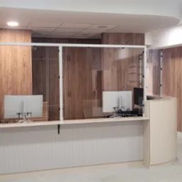 Nowoczesne wnętrze biurowe z drewnianymi panelami ściennymi, przeszklonym stanowiskiem recepcyjnym z dwoma monitorami i trzema krzesłami dla oczekujących gości.